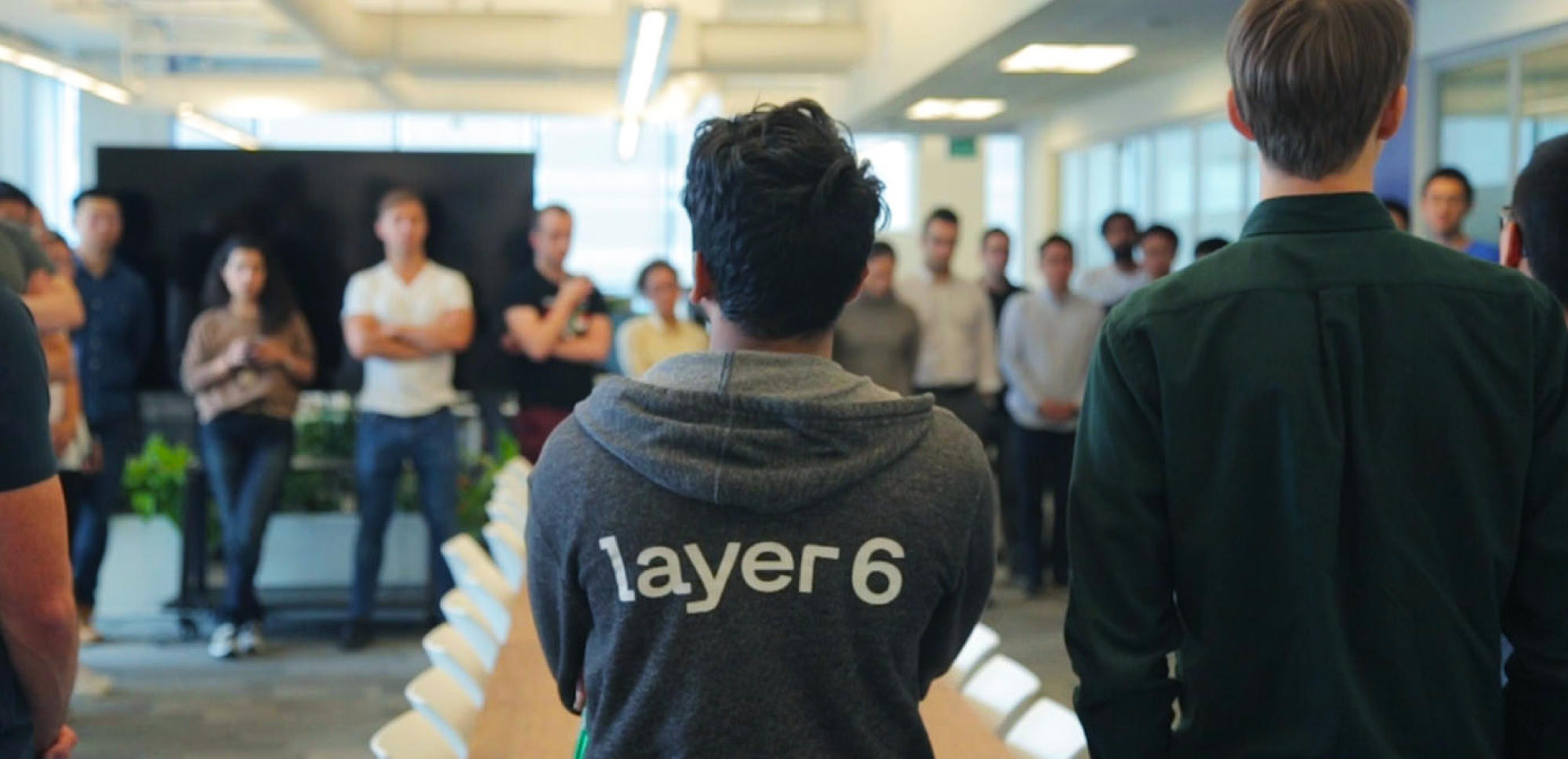 Team stand-up meeting with team member wearing Layer 6 logo design on a hoodie
